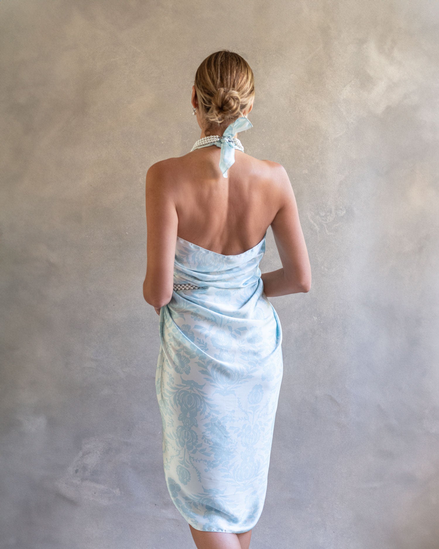 Elegant back view of a woman wearing a sky blue sarong pareo, showcasing the flowing fabric and wrap design in a serene studio environment