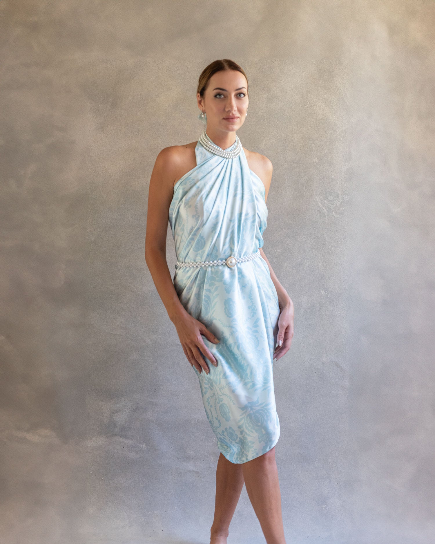 Front view of a woman in a light ethereal sky blue pareo styled as a wrap dress, standing confidently in a natural light setting