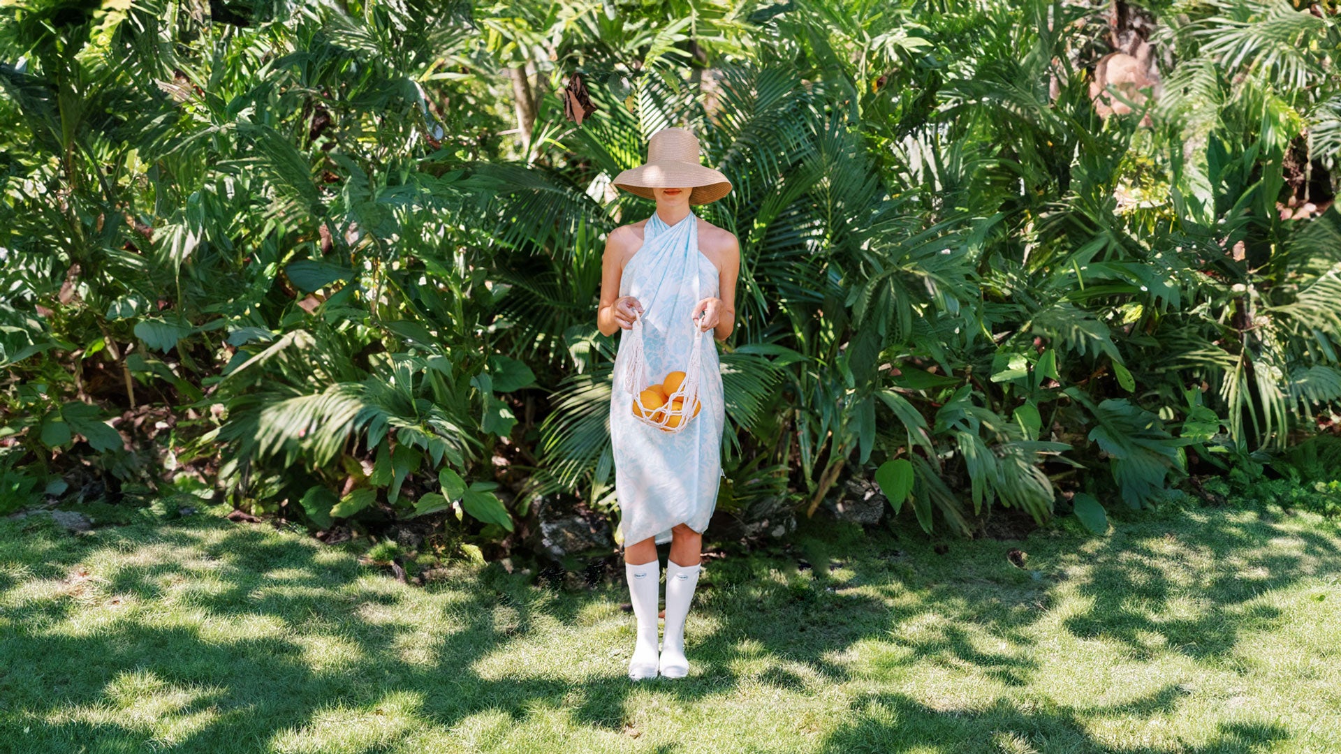 Woman in a light blue pareo and retro hat, creating a sophisticated and timeless look as she holds fresh oranges, evoking a sense of summer abundance