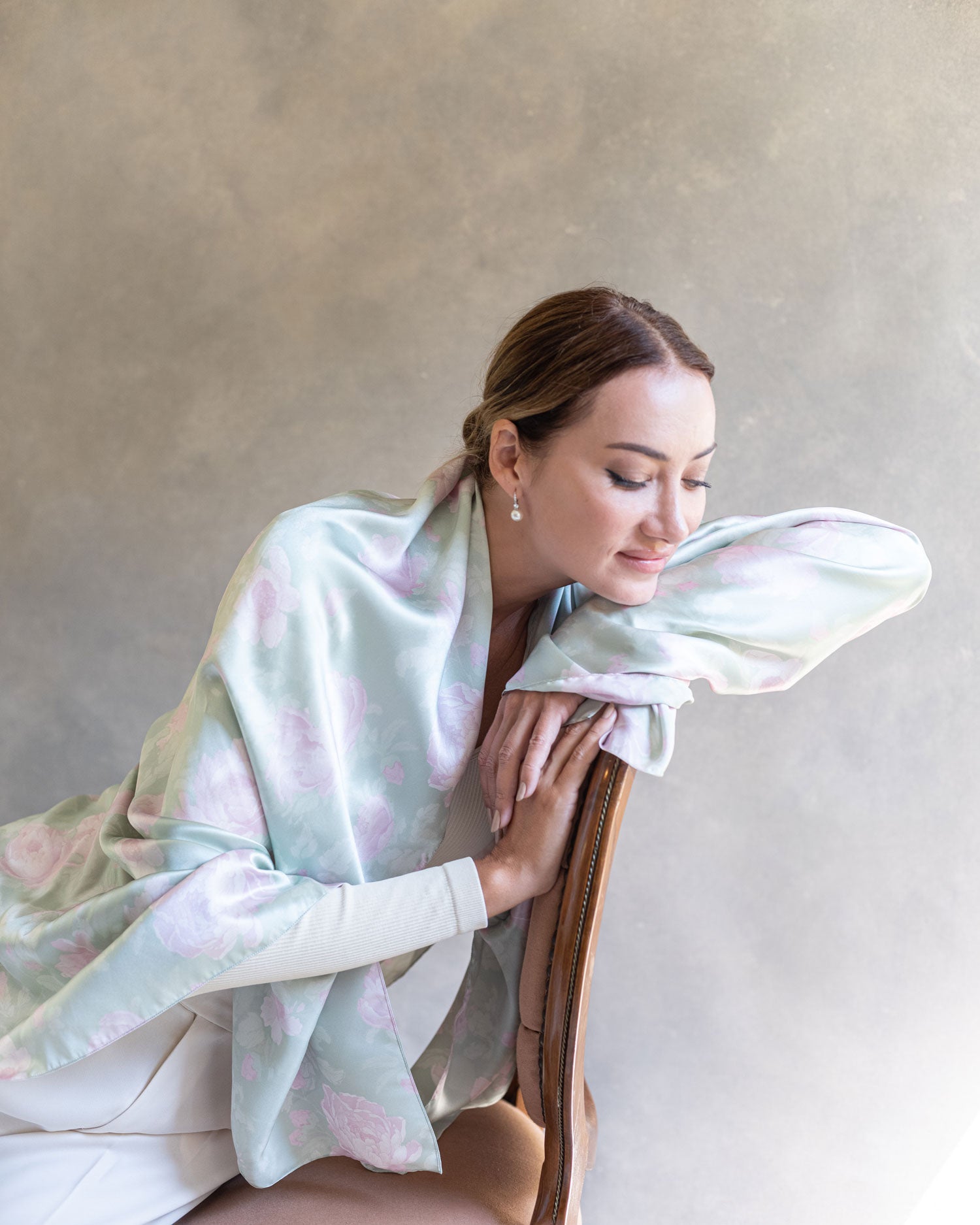 Close-up of a woman seated in an antique chair, the elegant drape of the light jade green pareo with pink roses visible as she looks down introspectively