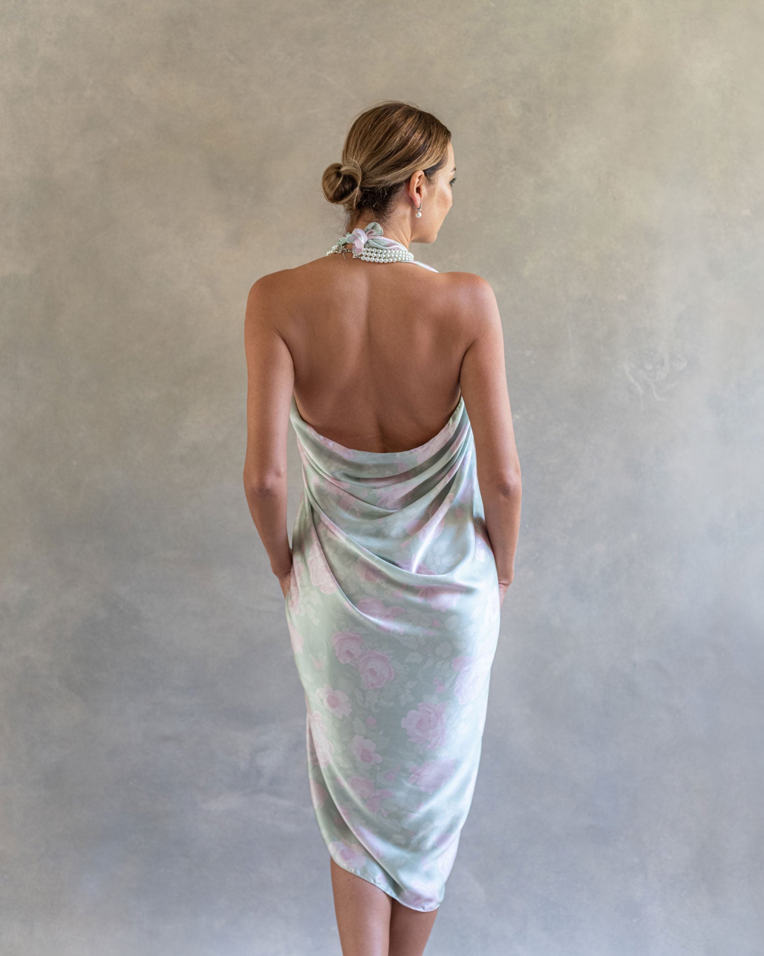 Elegant back view of a woman wearing a jade green sarong pareo, showcasing the flowing fabric and rose design in a studio setting