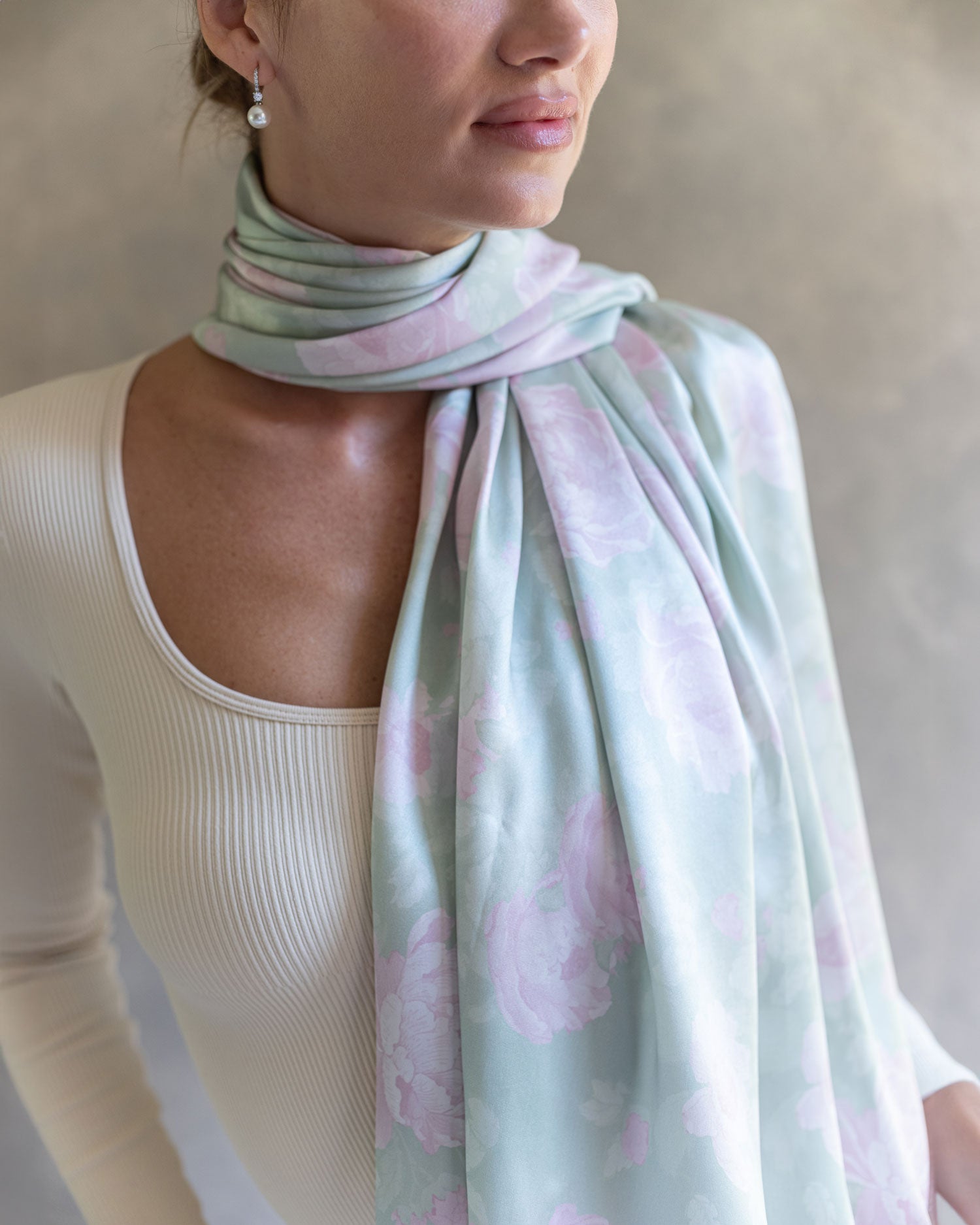 Close-up of the light jade green pareo wrapped as a scarf around the woman's neck, highlighting the intricate rose pattern