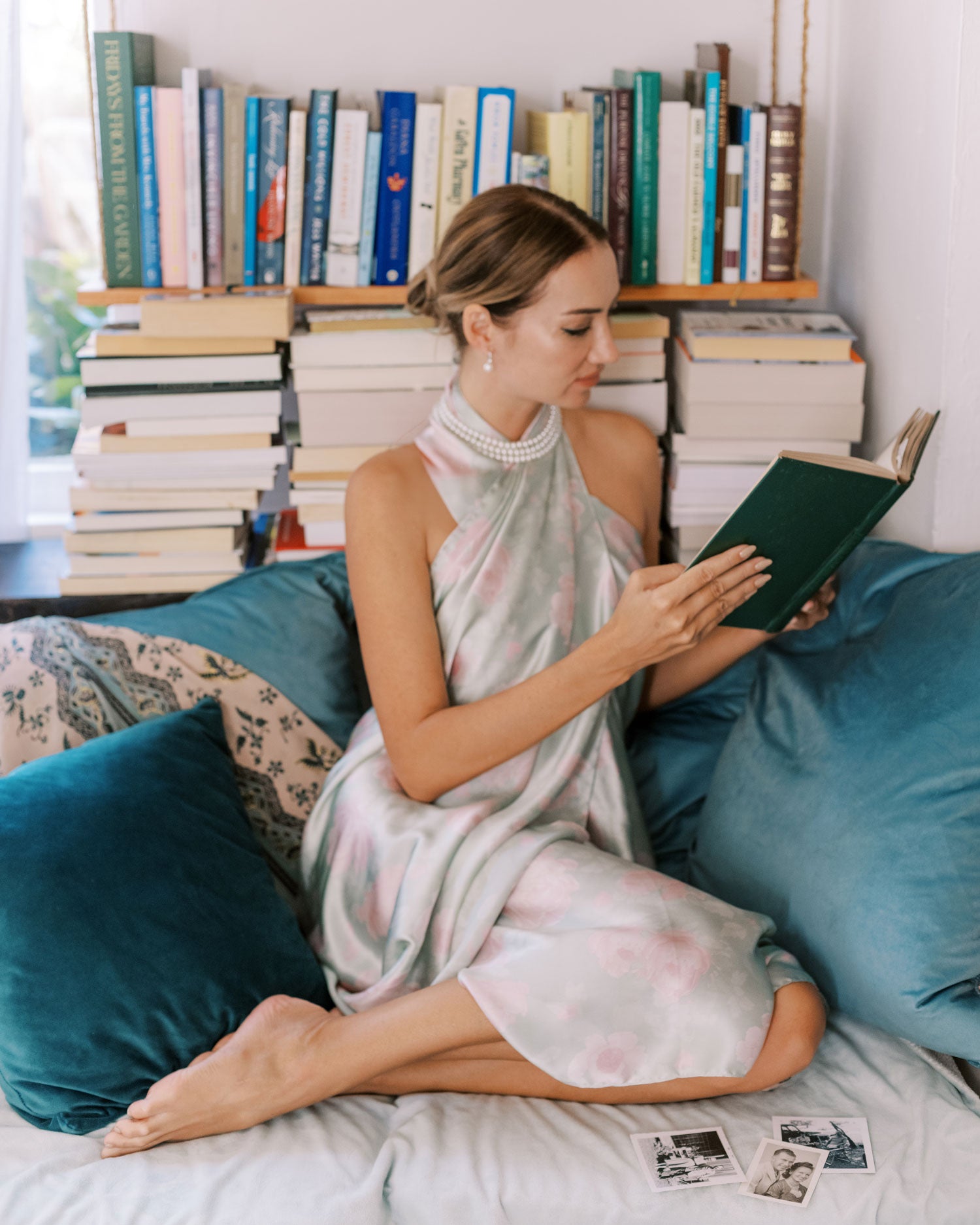 Image of a woman reading a book in a cozy nook, surrounded by a small personal library and comfortable pillows, her jade green pareo draped casually