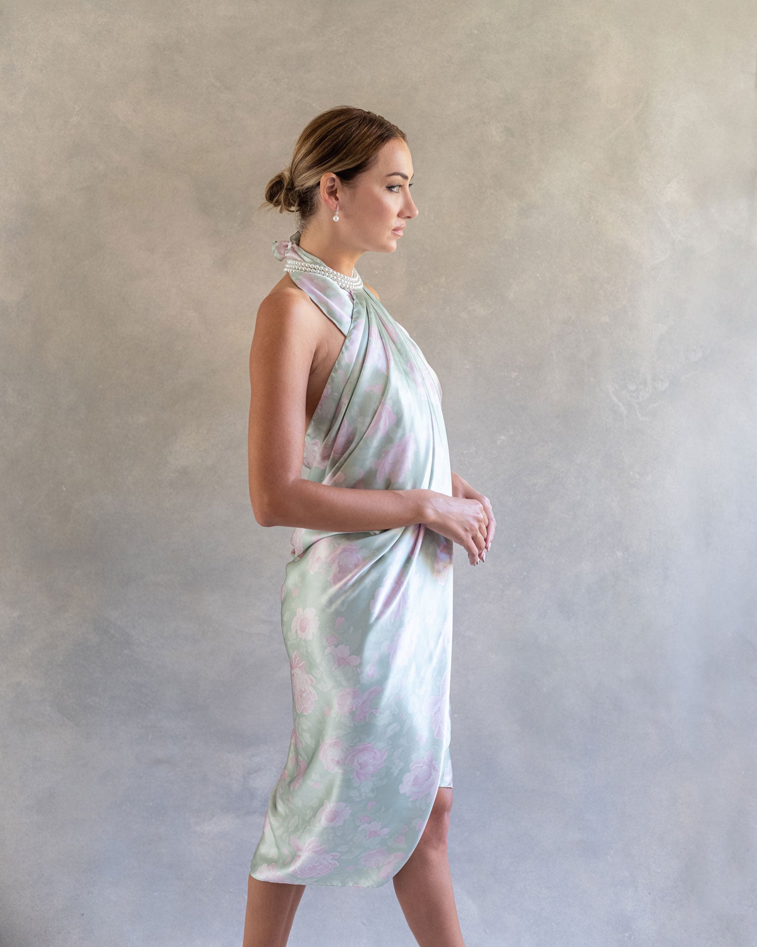 Side profile of a woman in a jade green pareo sarong dress, the pastel pink rose print enhancing the ethereal drape of the fabric