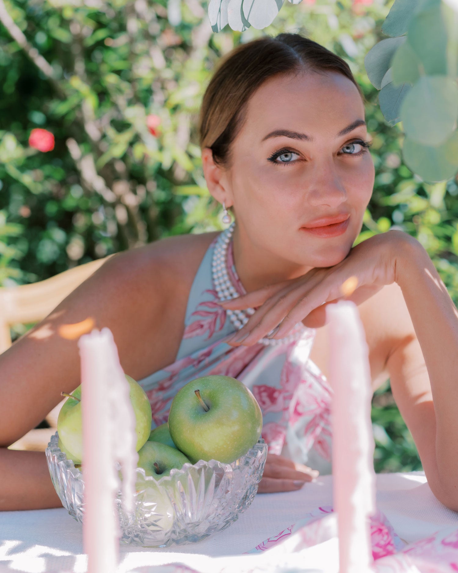 Close up of stylish woman wearing sarong styled as a dress with pink and blue pattern, serene pose with garden in background and outdoor table with candles in foreground