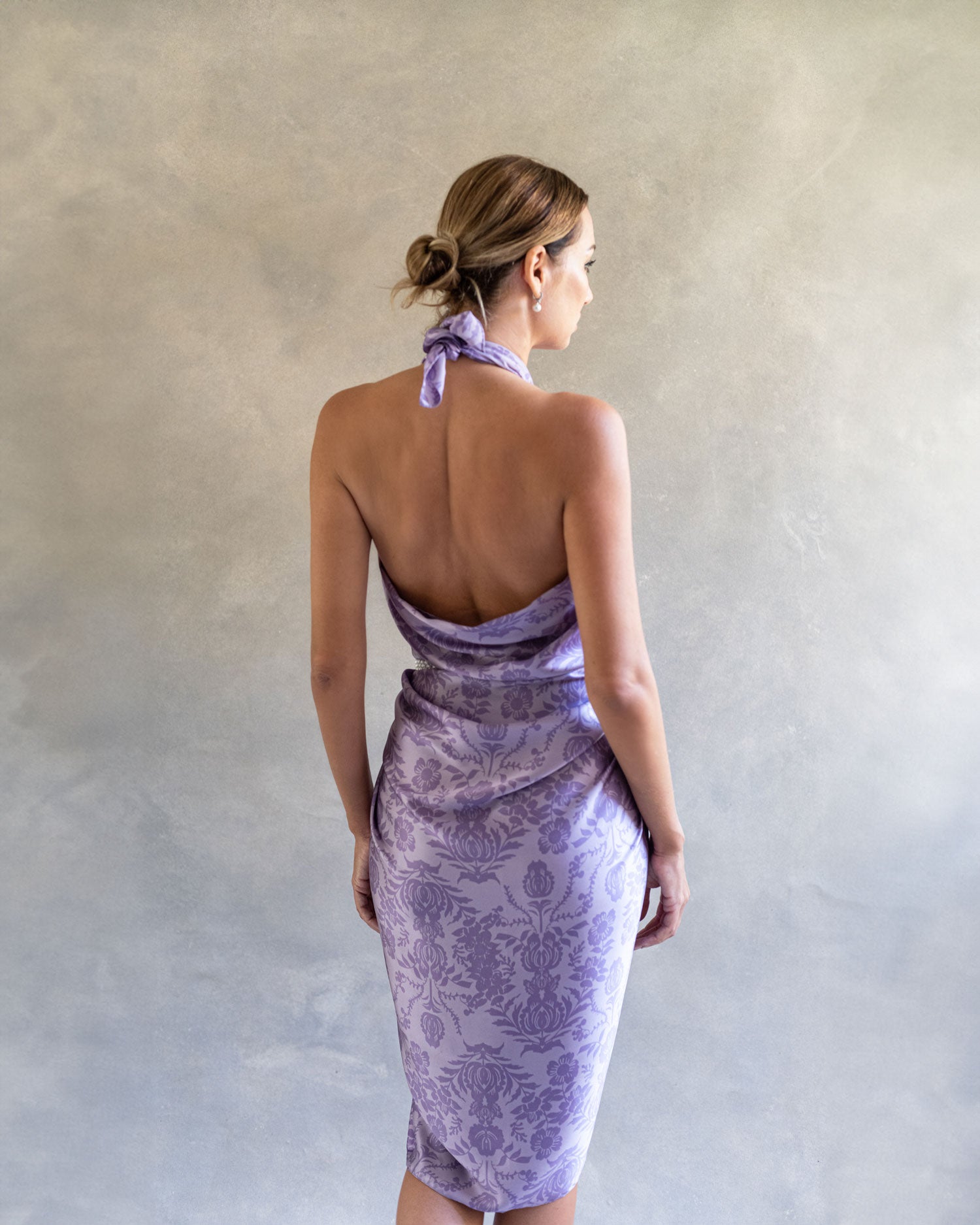 Back view of a woman wearing a chic purple lavender sarong pareo, tied as a dress in a studio environment