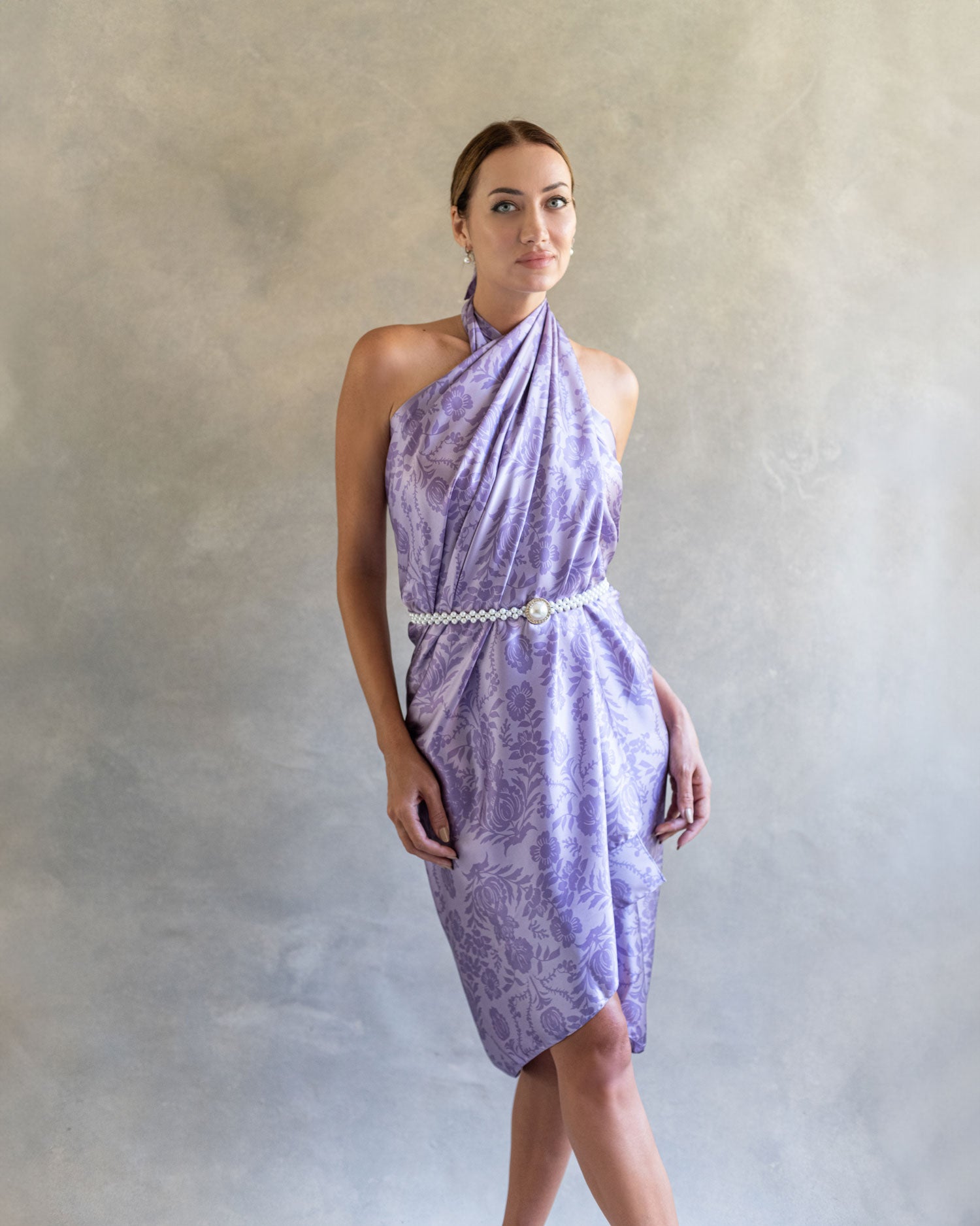 Front view of a woman in a purple lavender patterned pareo styled as a wrap dress, standing in a studio.