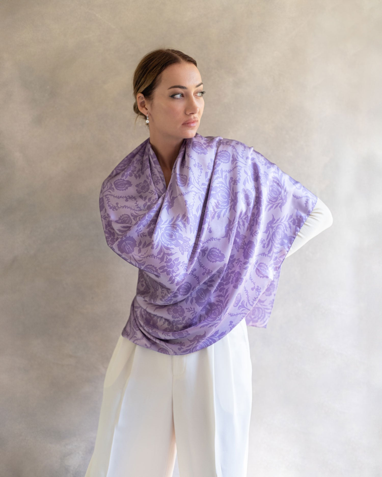 Artistic shot of a woman draped in a purple lavender pareo as a shawl, contrasted against subdued grey background