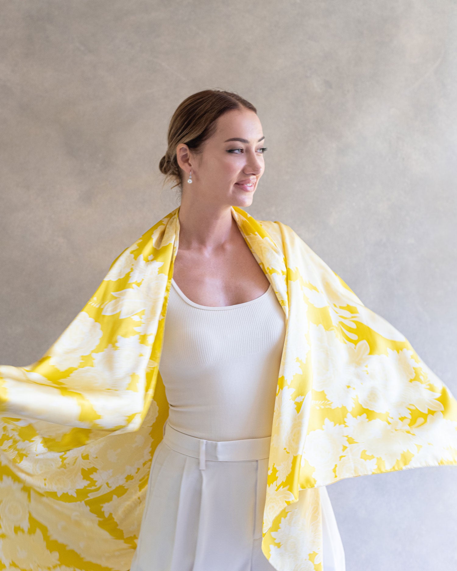 Happy woman using a bright yellow pareo sarong as a shawl, showing the elegant drape and movement of the silk fabric