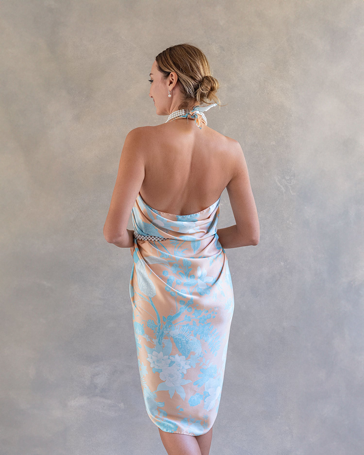 Back view of a woman wearing a vibrant orange and blue sarong pareo, tied as a dress, the pattern in the style of Chinoiserie, in a studio setting