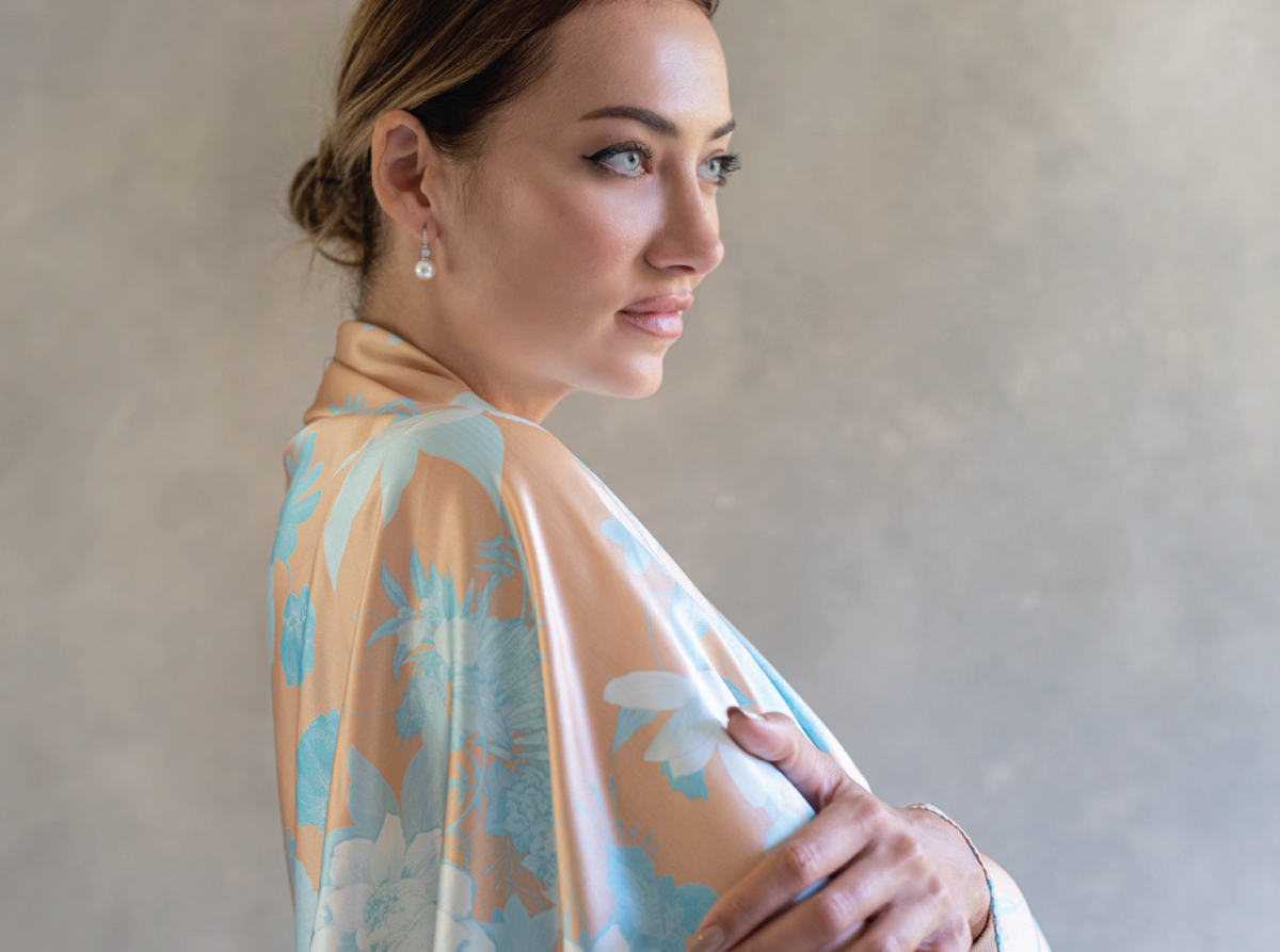 Side angle of a woman wearing an orange and blue pareo as a shawl, its hues complementing the minimalist studio environment